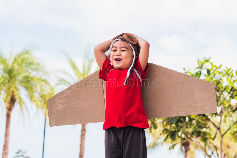 Kid little boy smile wear pilot hat and goggles play toy cardboard airplane wing flying