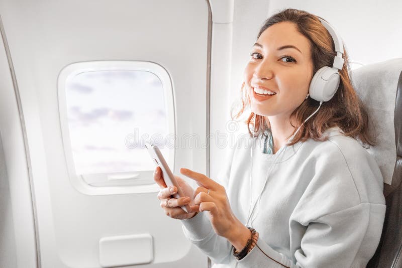 Asian girl with headphones listening music by smartphone while travelling by airplane