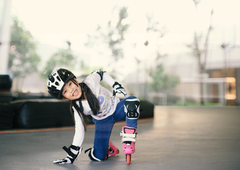 Happy Asian girl learning to roller skate. Children wearing protection pads for safe ride. Active outdoor sport for kids