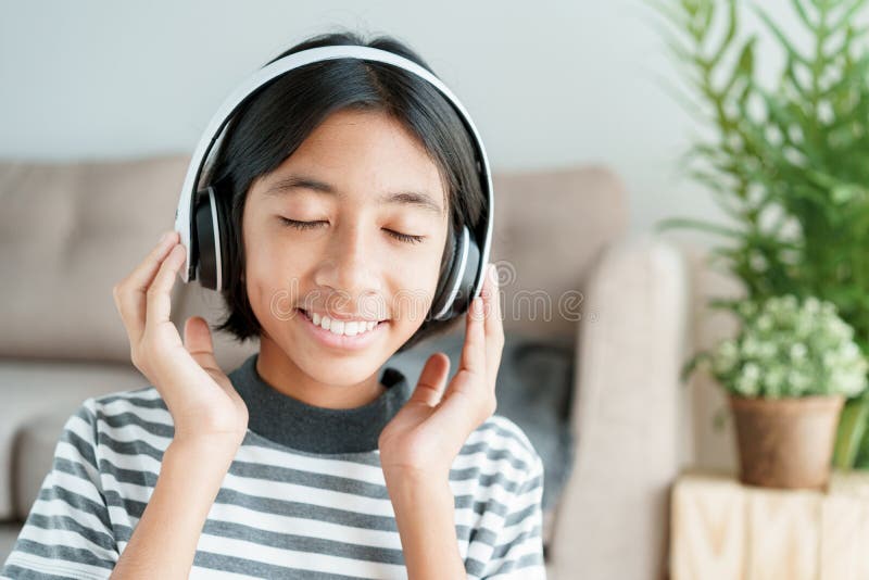 Happy Asian girl is music while sitting in the living room with closed eyes, Close-up expression on the child face and smile. Confidence. Concept of relaxation royalty free stock photo Happy Asian girl is music while sitting in the living room with closed eyes, Close-up expression on the child face and smile. Confidence. Concept of relaxation royalty free stock photo
