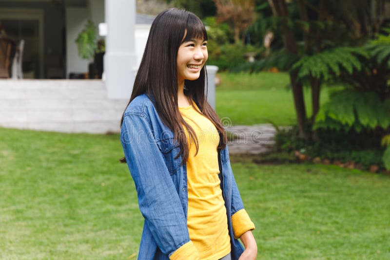 Happy asian girl smiling outdoors in garden outside family home wearing casual clothes