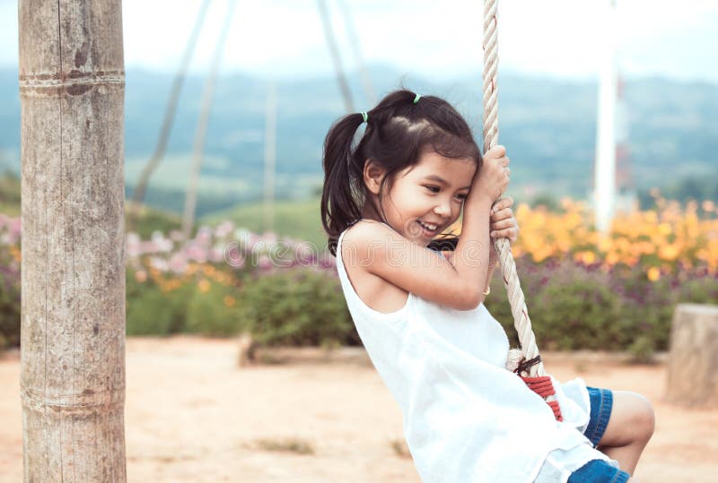 Happy asian little child girl having fun to play on wooden swings
