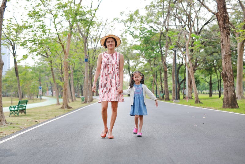 Happy Asian mom and daughter walking on street in the summer park.