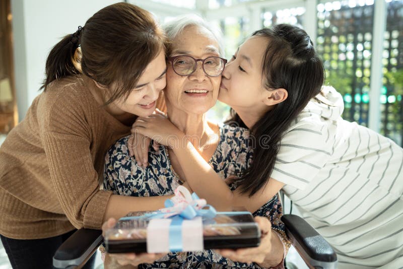 Happy asian mother,daughter meeting old grandparent,giving grandmother a gift,hugging,female elderly hold  present box,woman,child