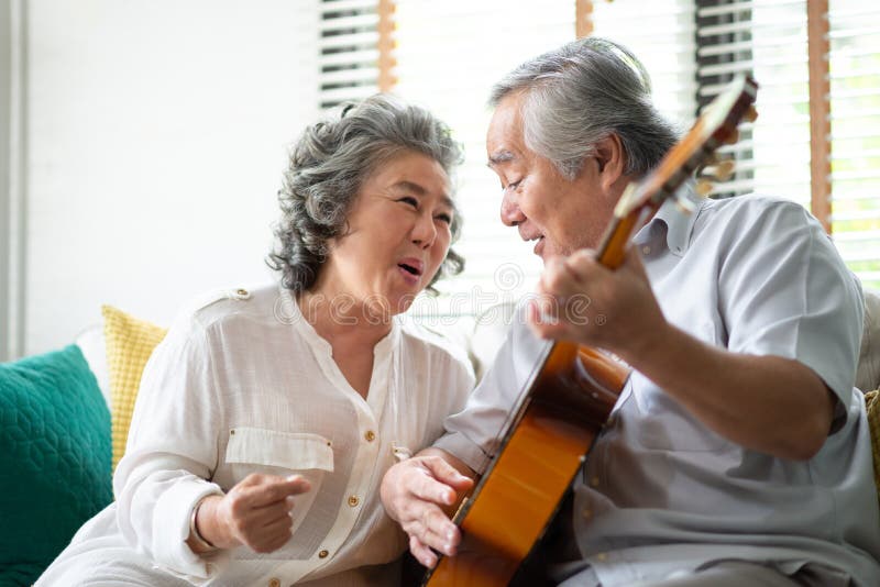 Happy Asian senior Couple enjoying with singing and playing guitar together. Having fun with the wedding Anniversary. Copy space