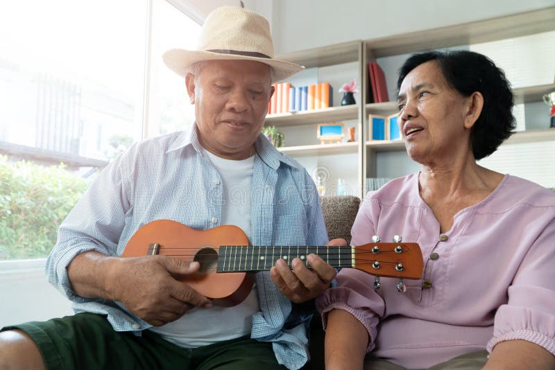 Happy Asian senior couple playing ukulele and singing together at home. The concept of life for the elderly after happy retirement.