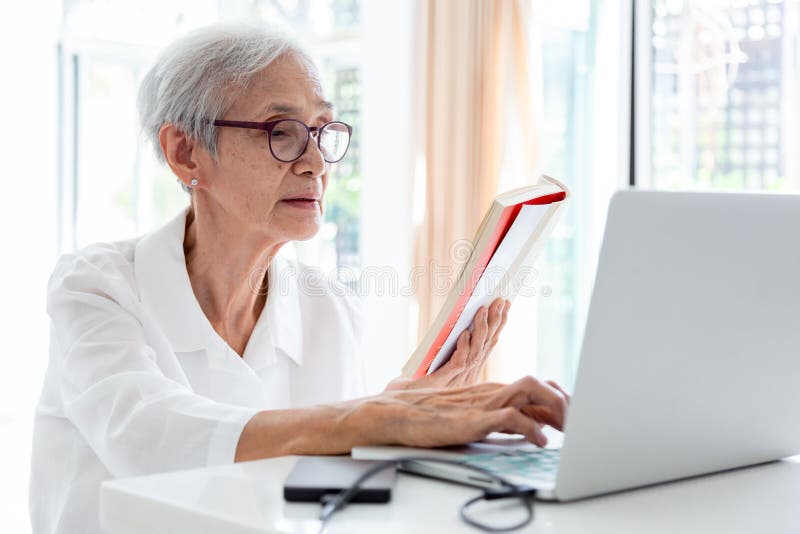Happy asian senior woman working,surfing the internet with laptop computer at table in home,smiling elderly people in glasses with stock photos Happy asian senior woman working,surfing the internet with laptop computer at table in home,smiling elderly people in glasses with stock photos