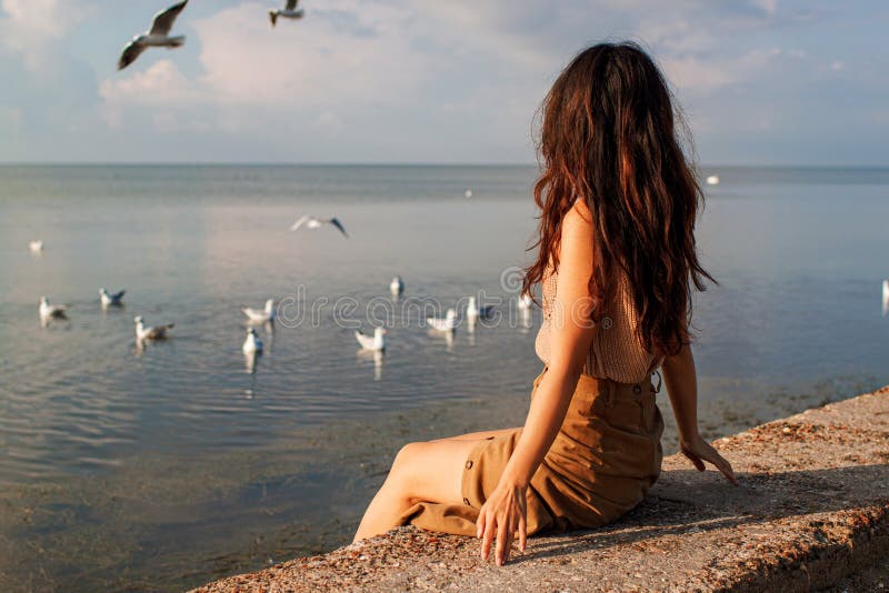 Happy Asian Woman With Arms Raised Standing At Beach Against Birds Flying In Clear Sky