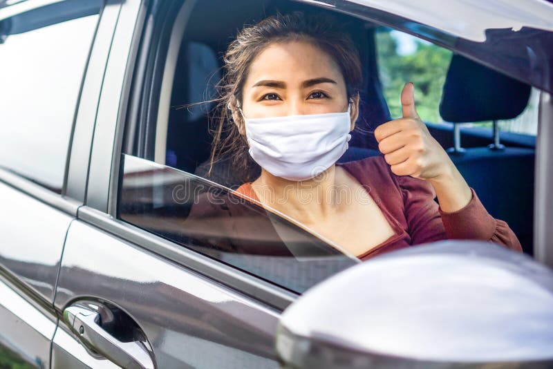 Happy Asian woman hand thump up and smiling in a car wearing protective mask before driving , covid-19 pandemic, new normal