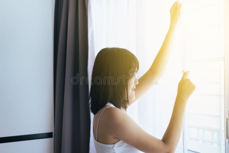 Happy of asian woman hands opening window curtainsafter wake up with bright morning sun