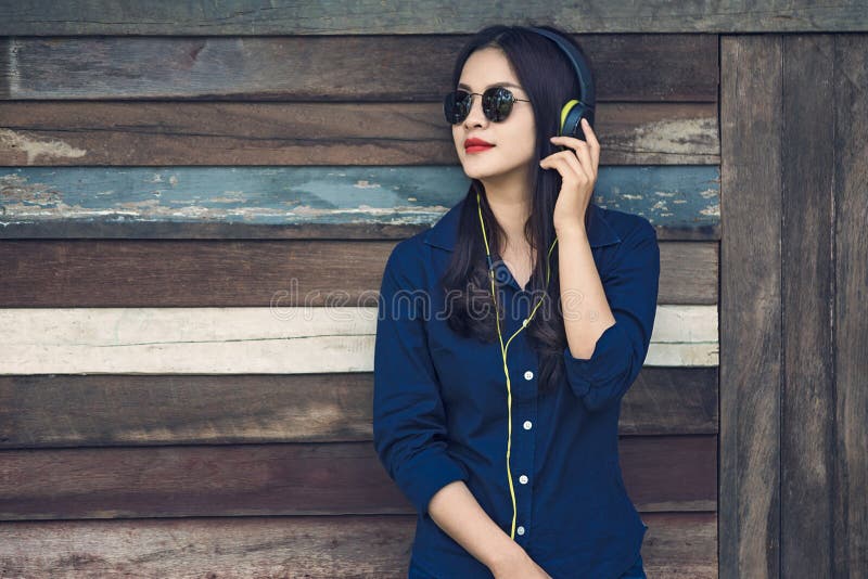 happy asian woman listening to music on her headphone and holding smartphone, leaning aginst old wooden barn wall, vintage retro stock photos happy asian woman listening to music on her headphone and holding smartphone, leaning aginst old wooden barn wall, vintage retro stock photos