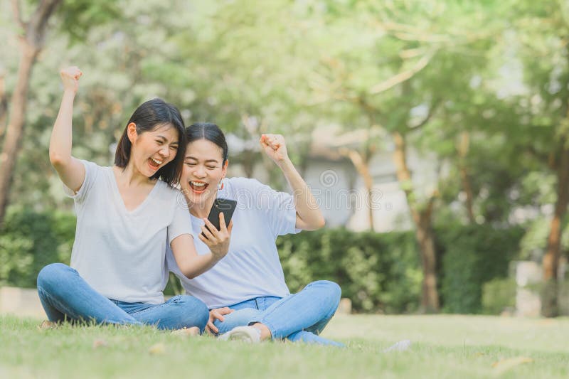 Women  celebrating success holding mobile phone sitting on grass