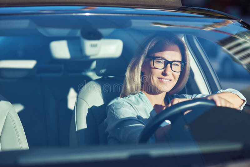 Happy attractive caucasian woman wearing eyeglasses driving her modern car through the city on sunny day, she is looking