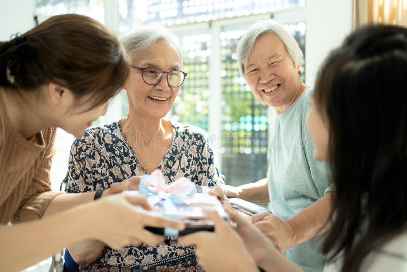 Happy-aziatische familie, dochter, kleindochter die op bezoek is en die een cadeau geeft aan oude grootouders, enthousiaste vrouw