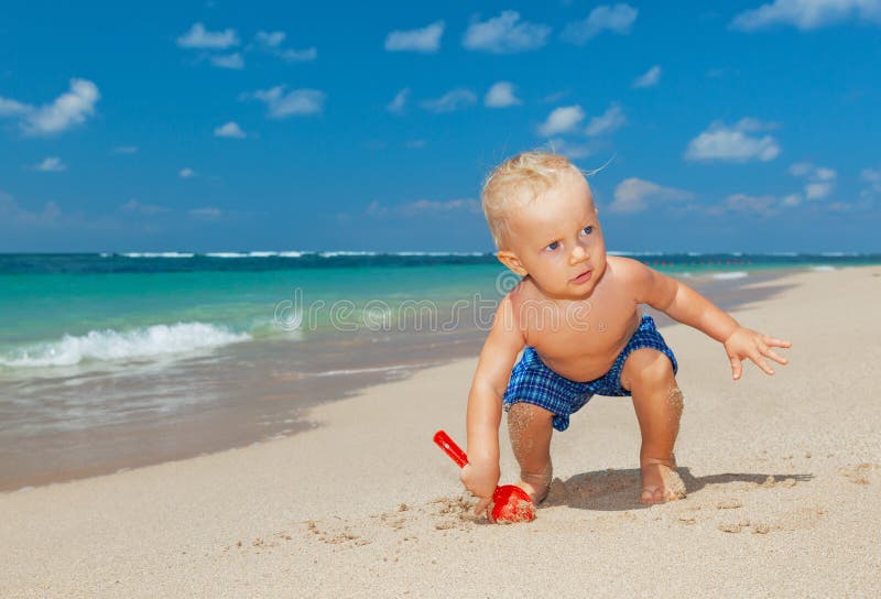 Happy baby boy digging sand on sunny tropical beach