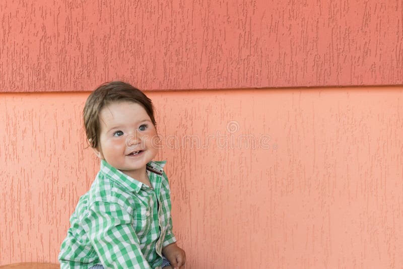 Happy baby on a coral background. Head and shoulders portrait of cute blue-eyed baby girl looking at camera and laughing on a royalty free stock photography Happy baby on a coral background. Head and shoulders portrait of cute blue-eyed baby girl looking at camera and laughing on a royalty free stock photography