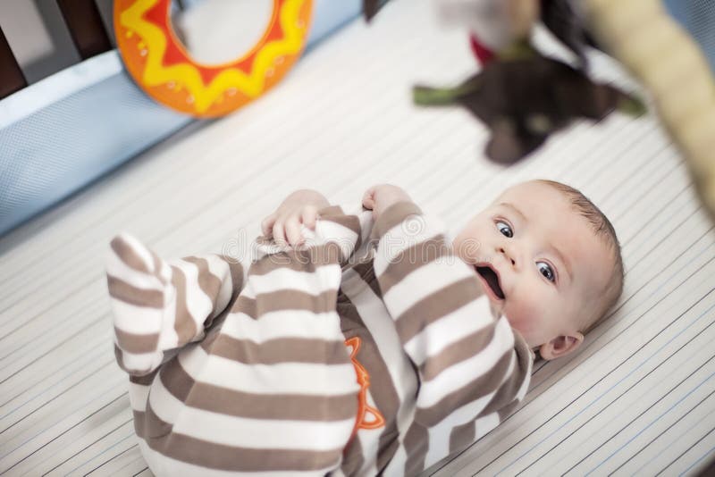 Sorridente bambino in culla a giocare con i suoi piedi.