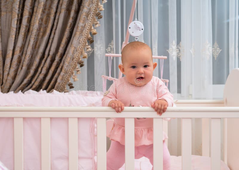 Happy baby girl in crib in pink bedroom scene.