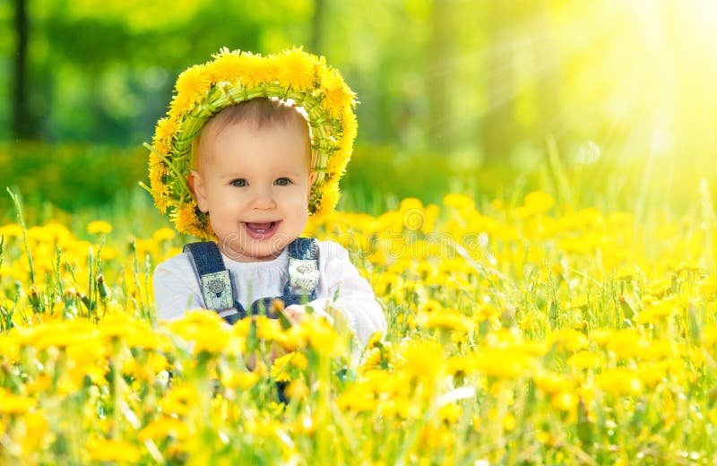 Happy baby girl in a wreath on meadow with yellow