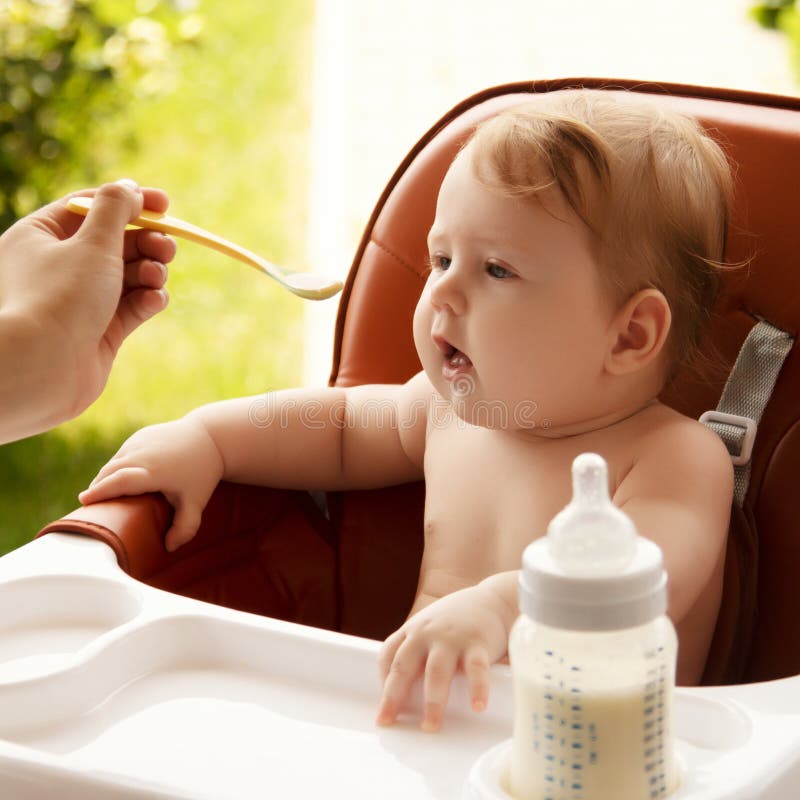 Happy Baby Sitting at the Table in the Kitchen and Eating with an