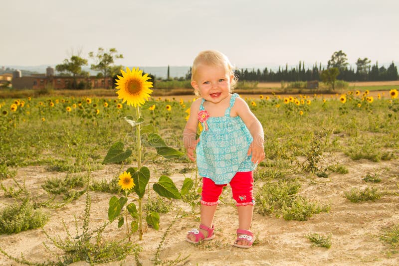 Happy baby standing next to sunflower