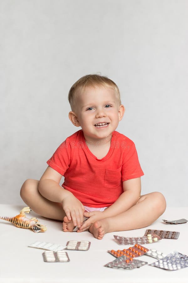 A happy baby Toddler in a live coral color T-shirt sits among the pills and drugs stock photos A happy baby Toddler in a live coral color T-shirt sits among the pills and drugs stock photos