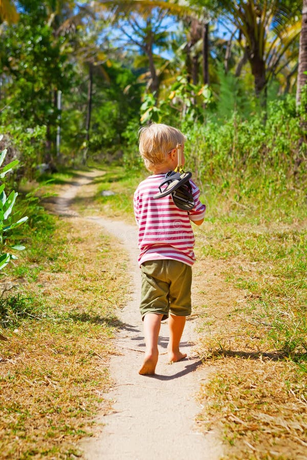 Happy barefoot child walk alone on beach by jungle path