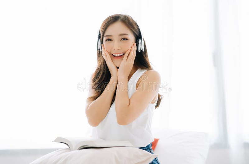 Happy beautiful Asian girl joyful listening to music using wireless earphones and holding her cheeks with a laugh looking to stock photography Happy beautiful Asian girl joyful listening to music using wireless earphones and holding her cheeks with a laugh looking to stock photography