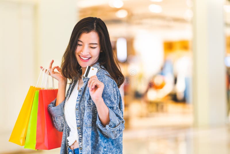 Happy beautiful Asian woman smile at credit card, hold shopping bags. Shopaholic people, retail special offer price concept