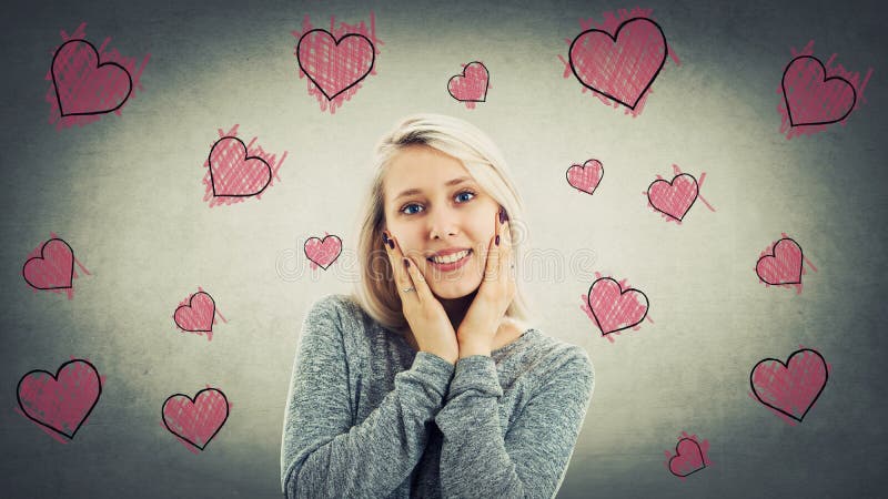 Happy beautiful girl holding her cheeks and laugh. Self love symbol as pink heart shape sketches floating around her head. Romantic valentine background.