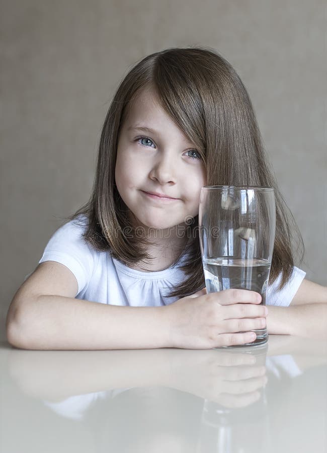 Happy beautiful little girl drinking clear water. Portrait of smiling baby holding transparent glass royalty free stock image Happy beautiful little girl drinking clear water. Portrait of smiling baby holding transparent glass royalty free stock image