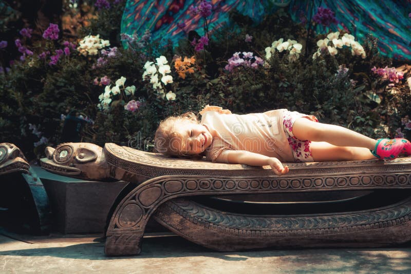 Happy beautiful smiling child girl lying on bench in blossoming flower garden with orchids concept childhood lifestyle royalty free stock image