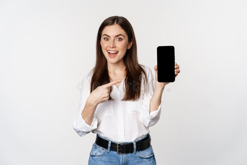 Happy beautiful woman smiling, pointing at mobile phone screen, showing advertisement, website, standing over white