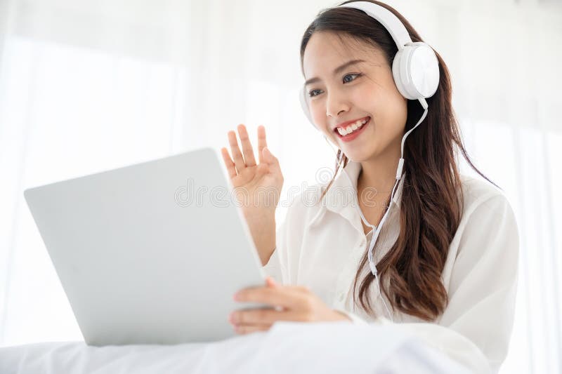 Happy beautiful young asian woman working on computer laptop and sitting on bed in house