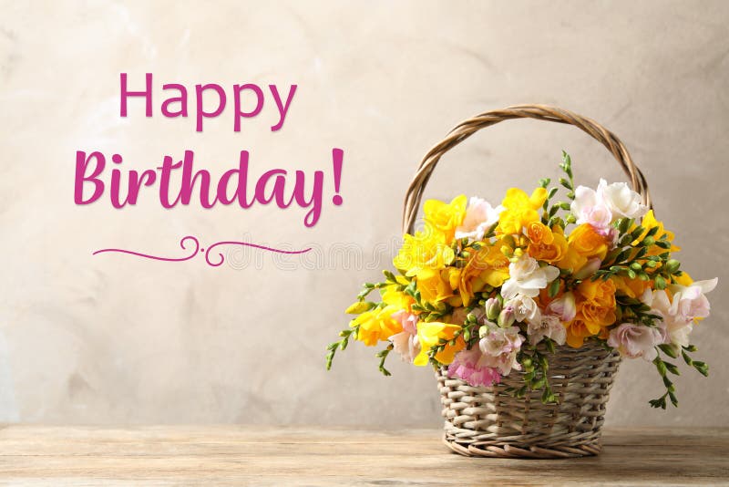 Happy Birthday! Beautiful freesia flowers in wicker basket on table