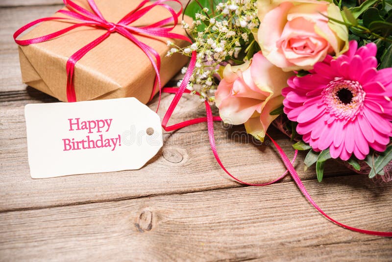 Bunch of flowers and tag with text on wooden background. Happy Birthday