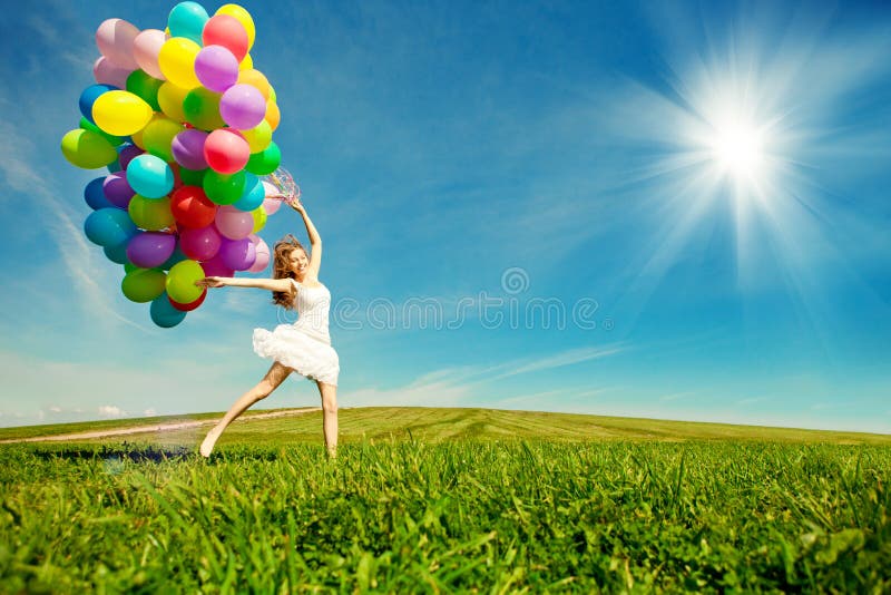 Happy birthday woman against the sky with rainbow-colored air balloons in hands. sunny and positive energy of nature. Young beautiful girl on the grass in the park.