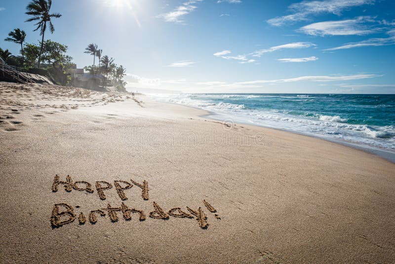 Happy Birthday written in the sand. On Sunset Beach in Hawaii with palm trees and the ocean in the background