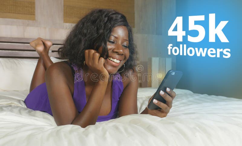 Happy black African American woman lying relaxed on bed using internet mobile phone smiling cheerful networking getting social stock image Happy black African American woman lying relaxed on bed using internet mobile phone smiling cheerful networking getting social stock image