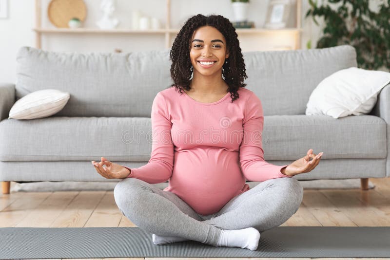 Happy black expecting lady meditating at home. Sitting on floor at living room royalty free stock image