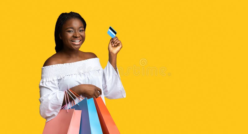 Happy black lady with shopping bags and credit card on yellow background