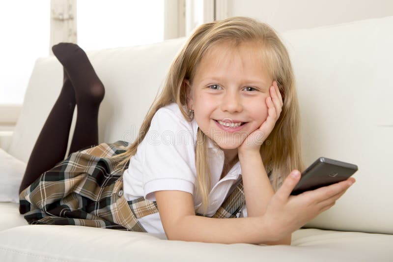 Happy blond little girl on home sofa using internet app on mobile phone