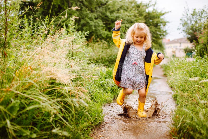 Happy blonde child girl in a yellow rubber boots and yellow raincoat jumping in a puddle. Summer, childhood, holiday stock images Happy blonde child girl in a yellow rubber boots and yellow raincoat jumping in a puddle. Summer, childhood, holiday stock images