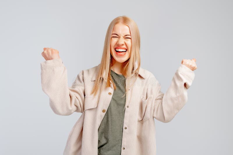 Happy blonde girl rejoicing her success and victory clenching her fists with joy. Lucky young woman being happy to achieve her aim