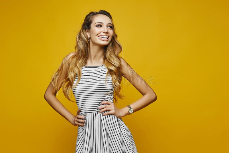 Happy blonde model woman with stylish hairstyle and beautiful smile in striped white dress posing at the yellow royalty free stock photography Happy blonde model woman with stylish hairstyle and beautiful smile in striped white dress posing at the yellow royalty free stock photography