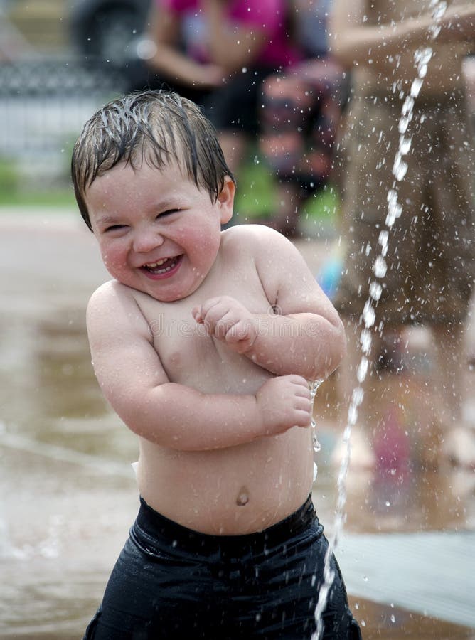 Baculaté malé batole, směje se, jak chladná voda šplouchá nad ním v létě splash podložka pod fontánu.