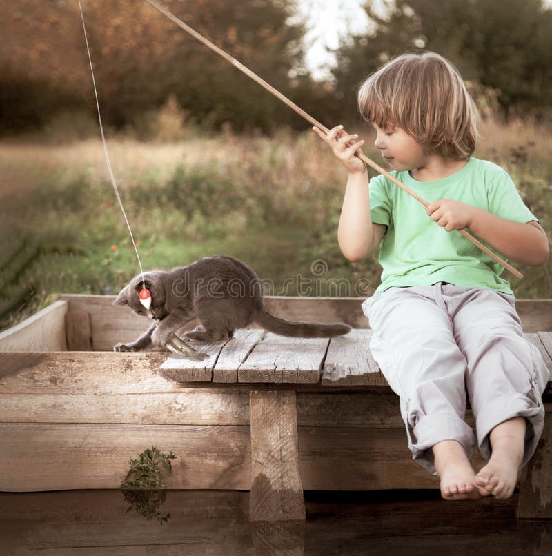 Happy boy go fishing on the river with pet, one children and kitten of the fisherman with a fishing rod on the shore of the lake