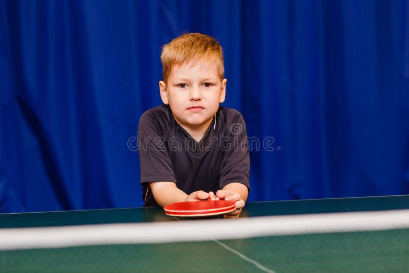 Happy boy in grey t-shirt and racket in hand on blue background. table tennis