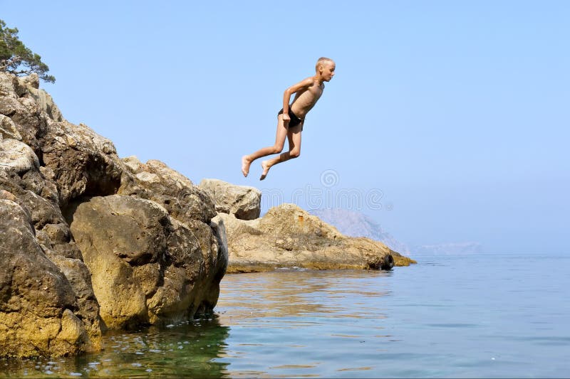 Happy boy jumps from rock into sea