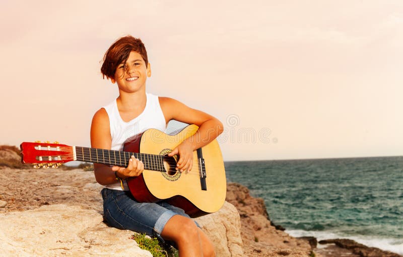 Happy boy playing guitar on the edge of a cliff stock photo Happy boy playing guitar on the edge of a cliff stock photo